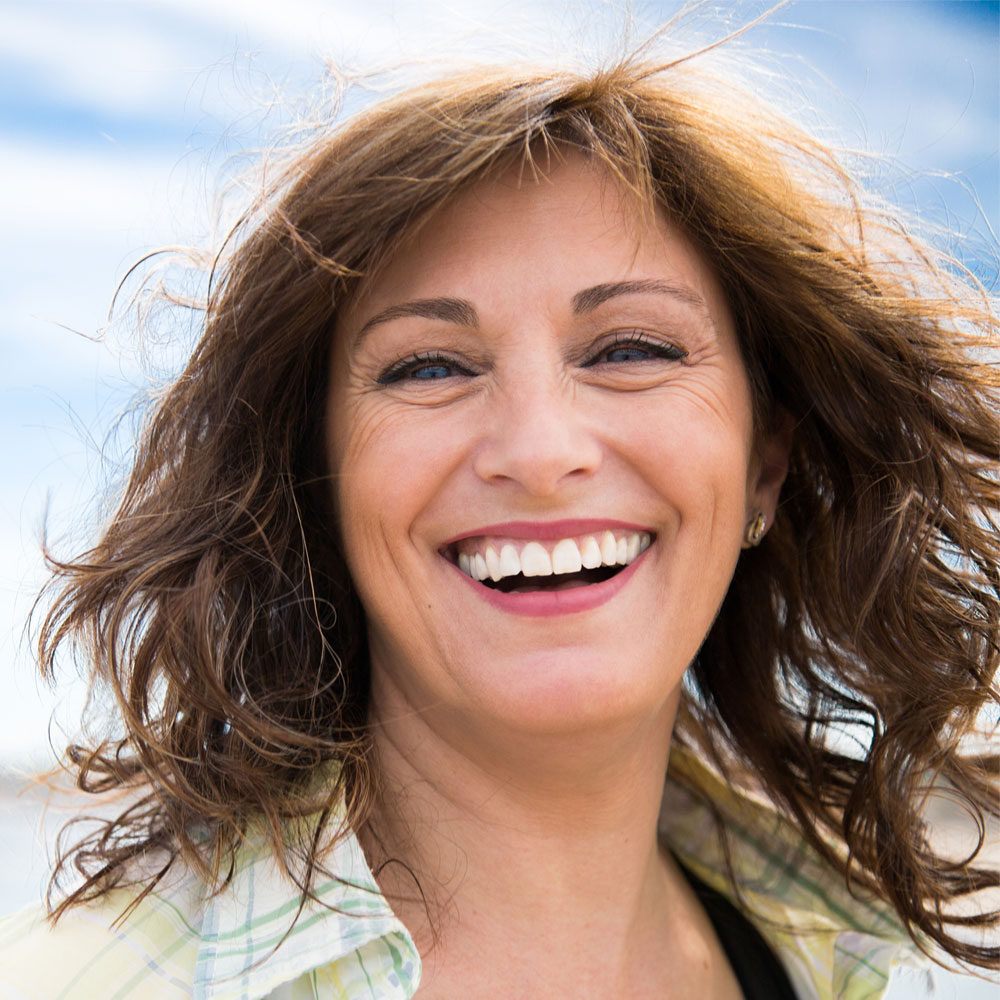 Elevation Med Spa Lone Tree Colorado smiling middle aged woman with hair blowing in the wind at the beach